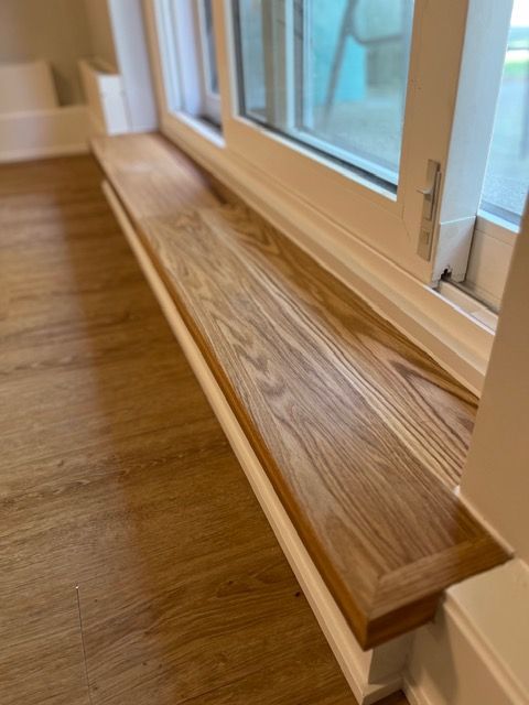 Wooden window sill in a room with wood flooring and white window frame.
