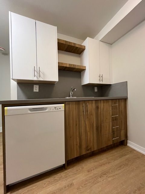 Small kitchen with white appliances and cabinets, wood-tone lower cabinets, grey countertop, and wooden shelves.