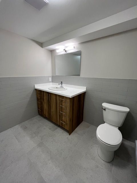 Bathroom with wood vanity, white countertop, mirror, and toilet. Gray walls and flooring.