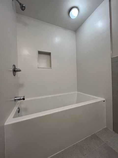 White bathroom with a tub, shower fixtures, and built-in wall niche.