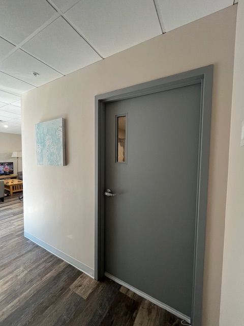 Gray door with window, hallway, artwork, and wood-look flooring.