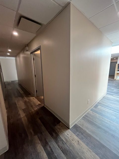 A hallway with a wooden floor and cream-colored walls, leading to a doorway and other rooms.