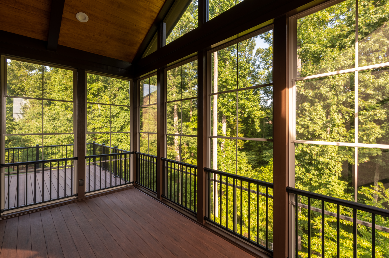 A screened in porch with lots of windows and trees in the background.