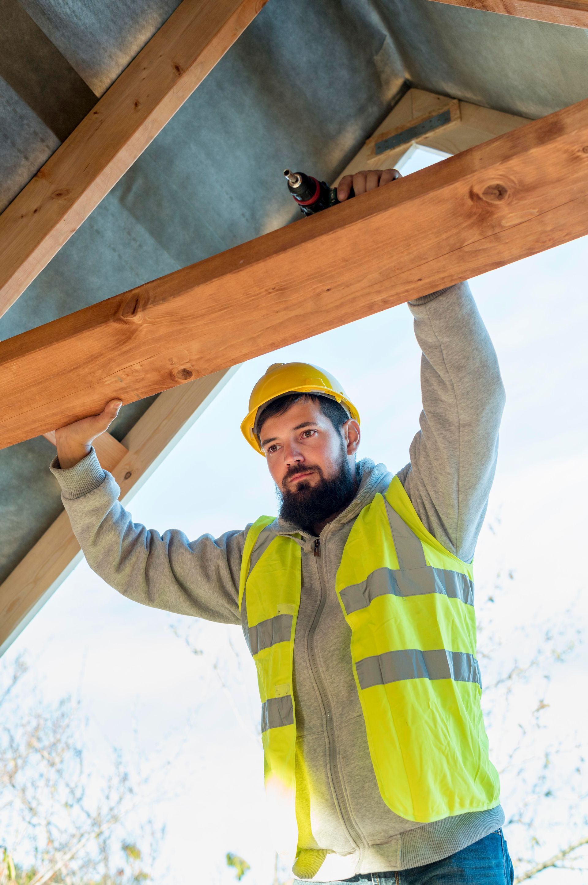 A construction worker is holding a wooden beam over his head.