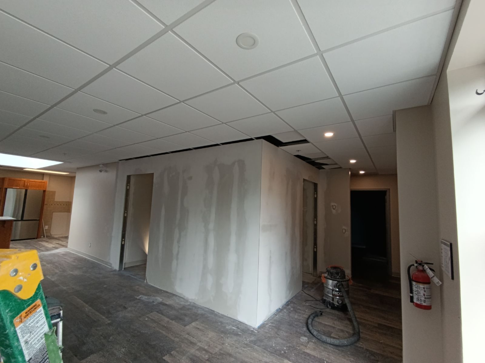 Interior of a room under construction with unfinished walls, drop ceiling, and exposed electrical work.