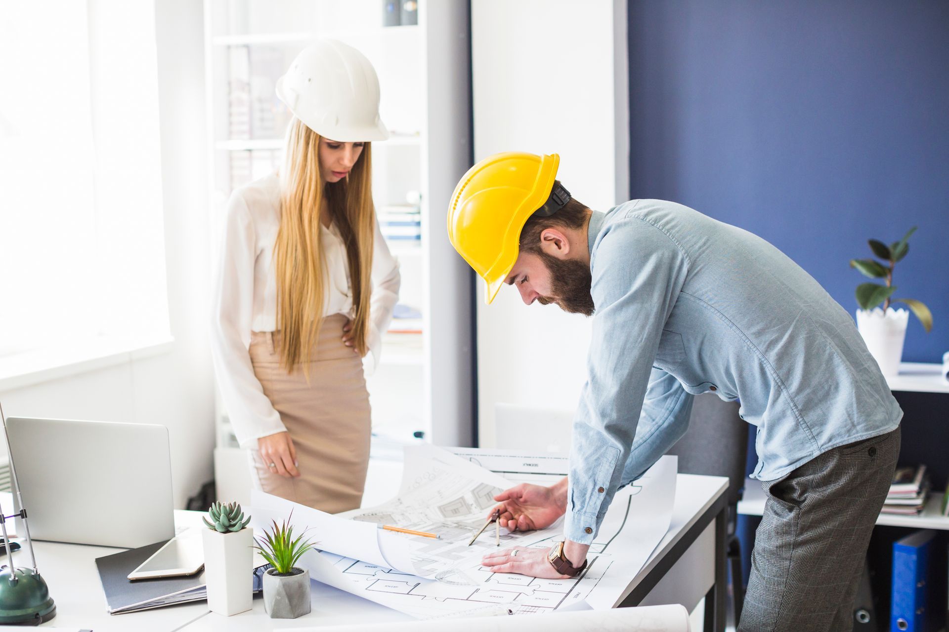 A man and a woman wearing hard hats are looking at a blueprint.