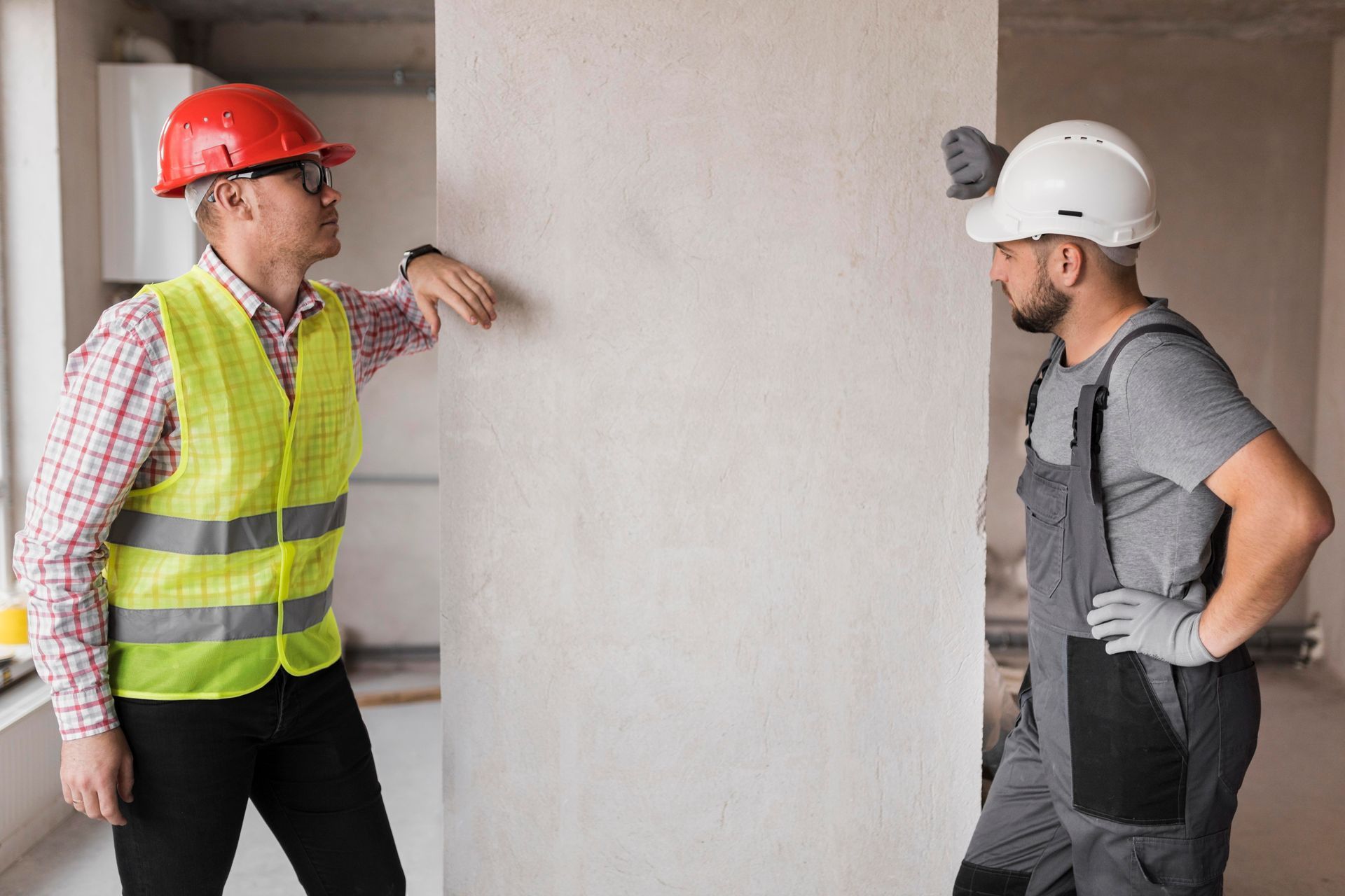 Two construction workers are standing next to each other in a room.