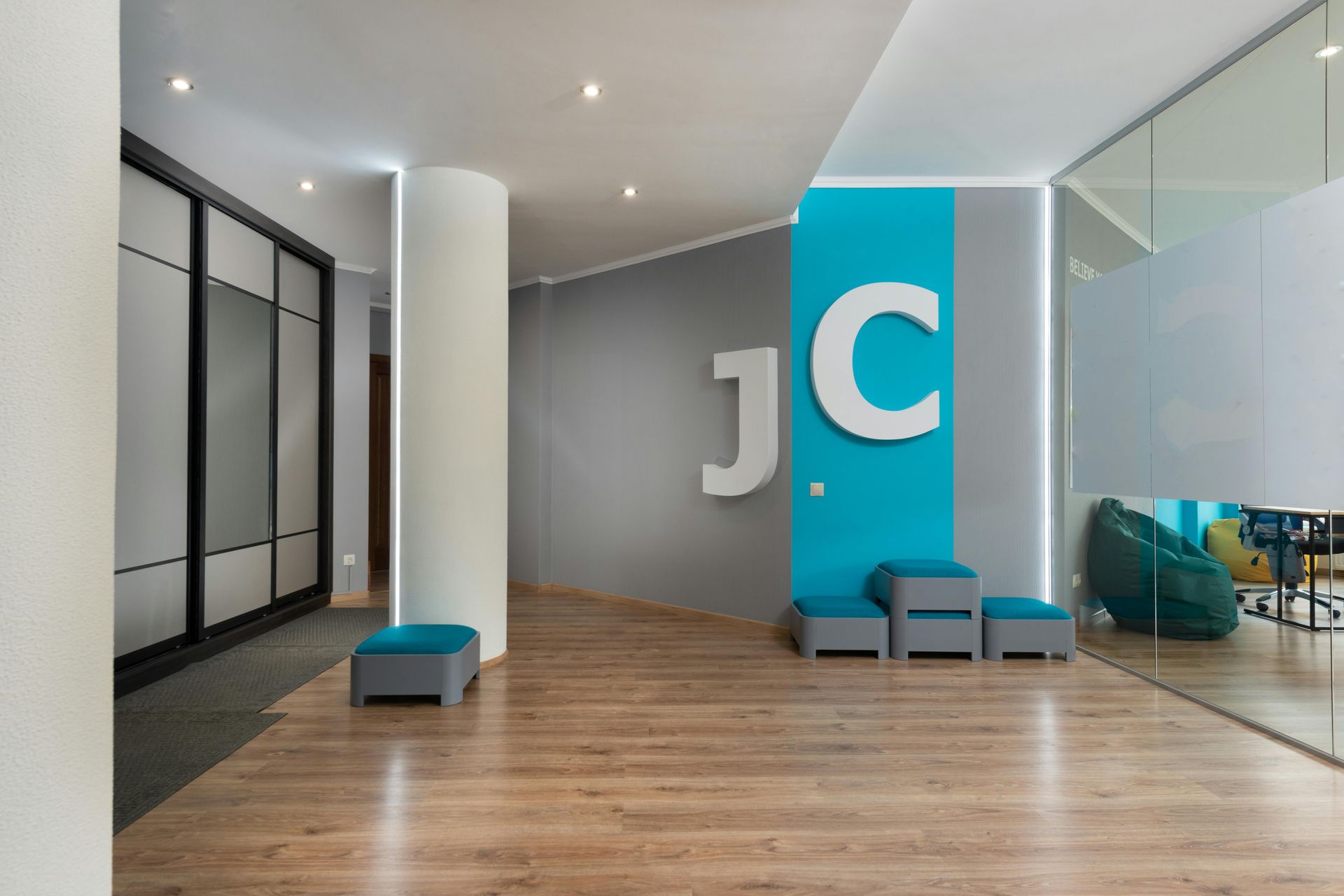 Modern office reception area with JC logo, gray walls, wooden floor, seating and a beanbag.