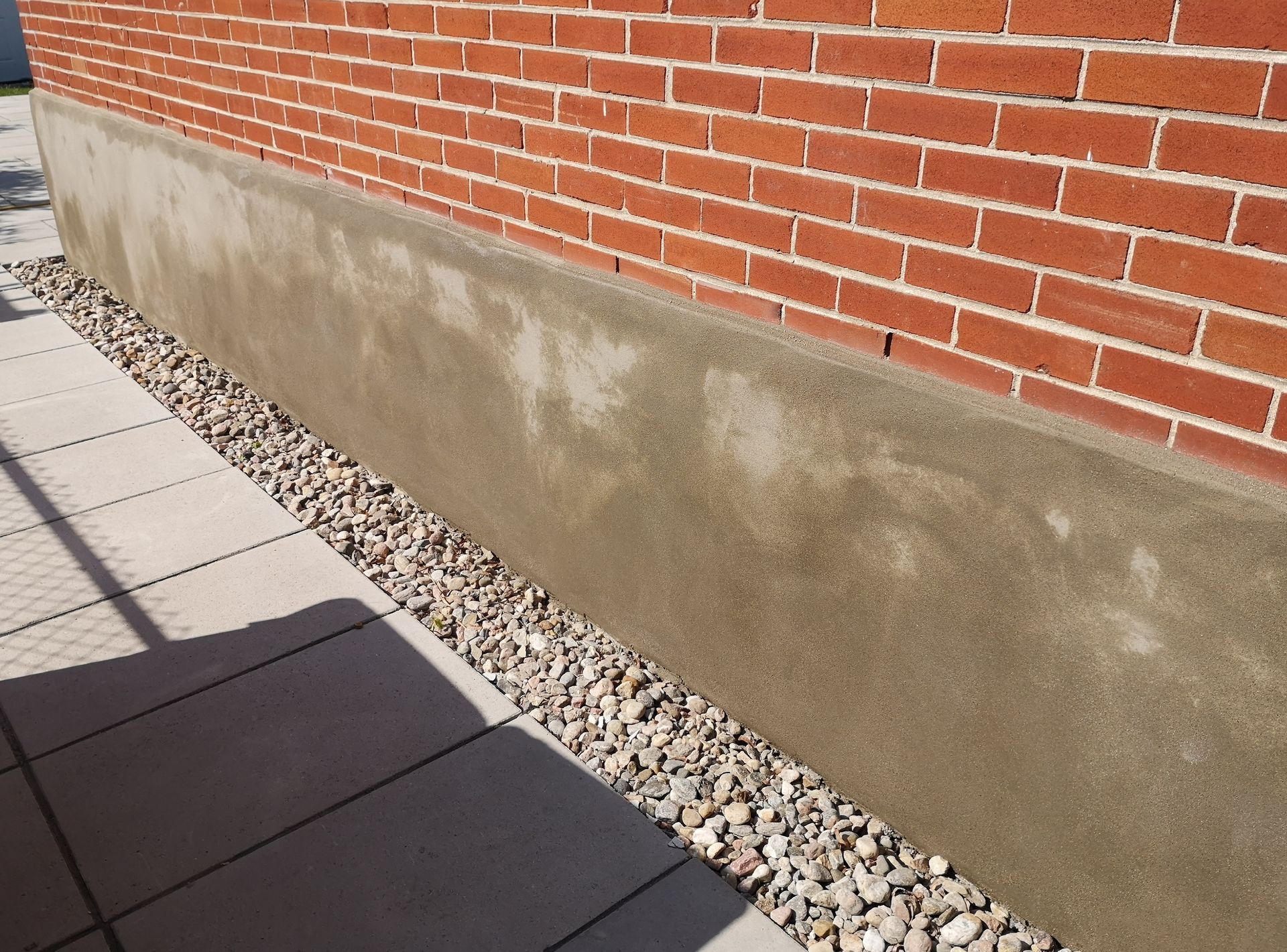 A brick wall with a concrete border and gravel on the sidewalk