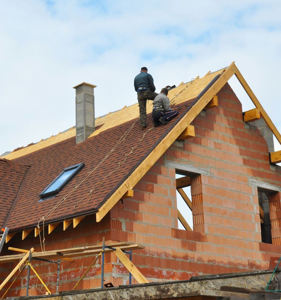 Two men are working on the roof of a brick house