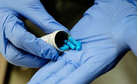 Hands in blue gloves holding a bottle of blue pills.