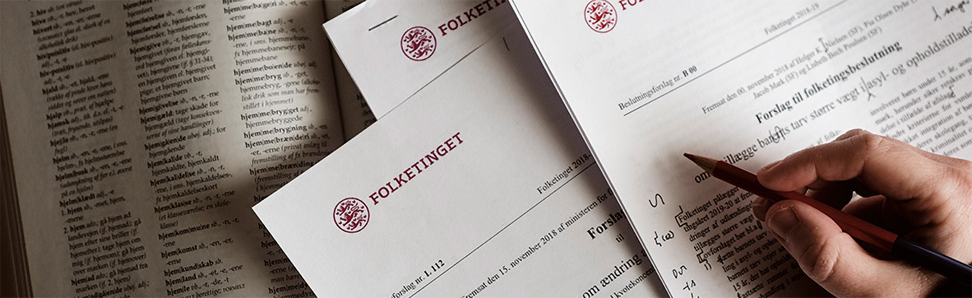 Hand writing on a document with red stamps, next to an open book.
