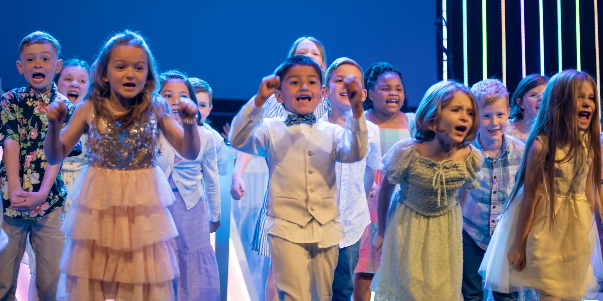 A group of children are standing on a stage singing and dancing.