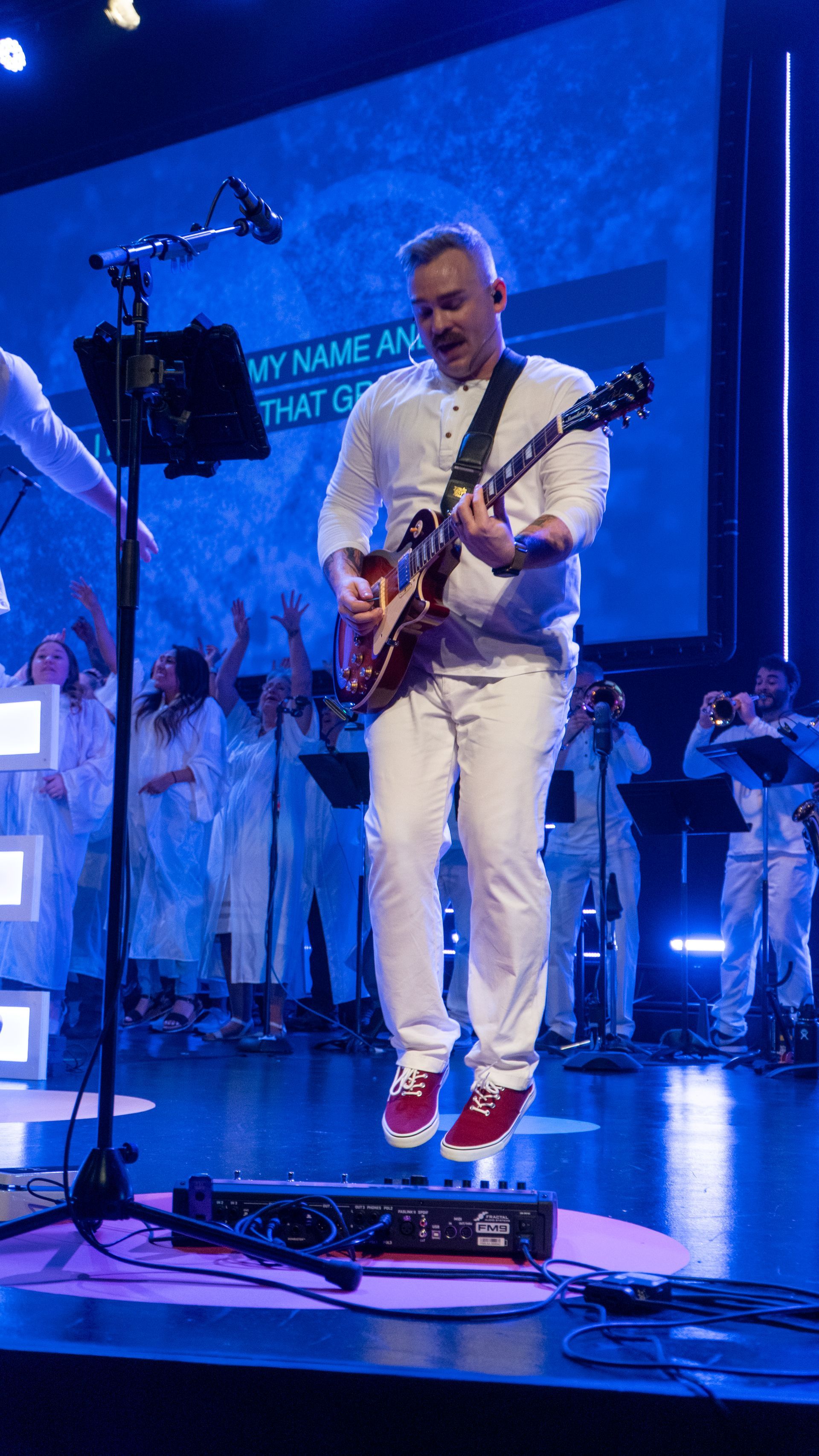 A man is jumping in the air while playing a guitar on a stage.