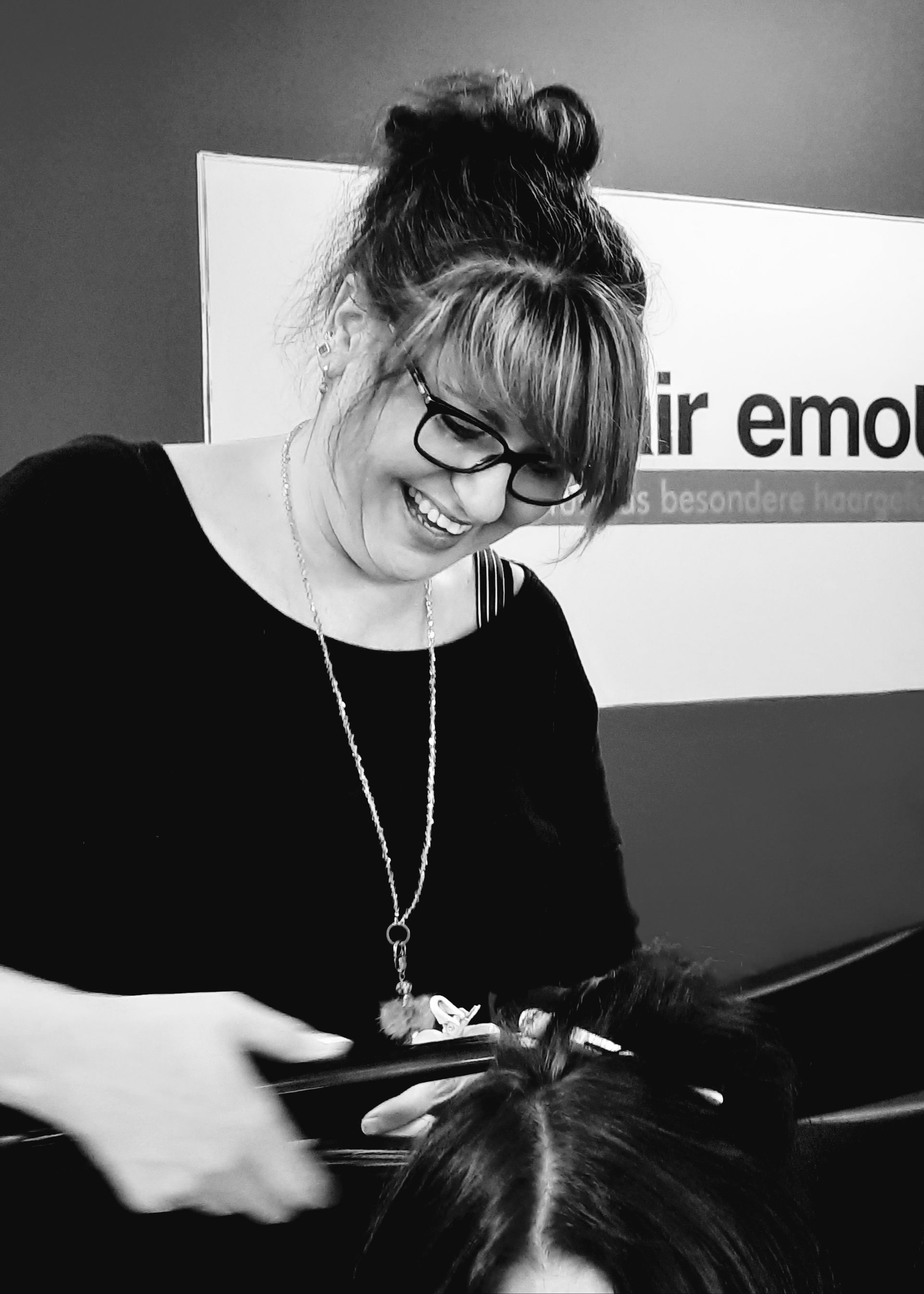 Eine Frau föhnt einer Frau die Haare vor einem Schild mit der Aufschrift „Emo“