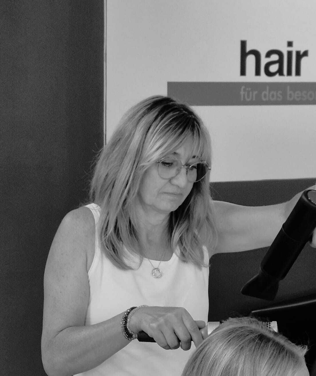Eine Frau schneidet sich die Haare vor einem Schild mit der Aufschrift „Haaremotion“