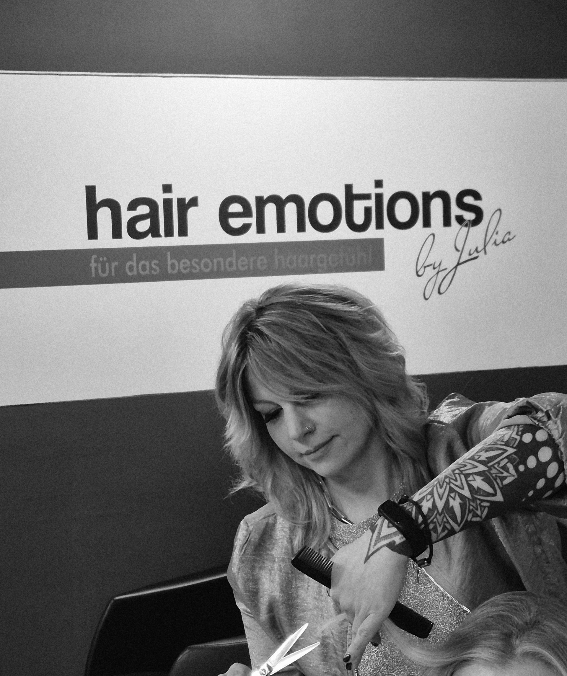 Eine Frau föhnt einer Frau die Haare vor einem Schild mit der Aufschrift „Emo“