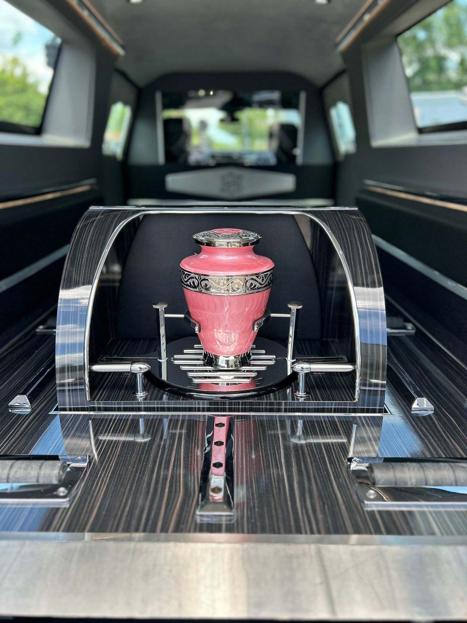 Pink urn inside a hearse. Shiny chrome accents, black interior.