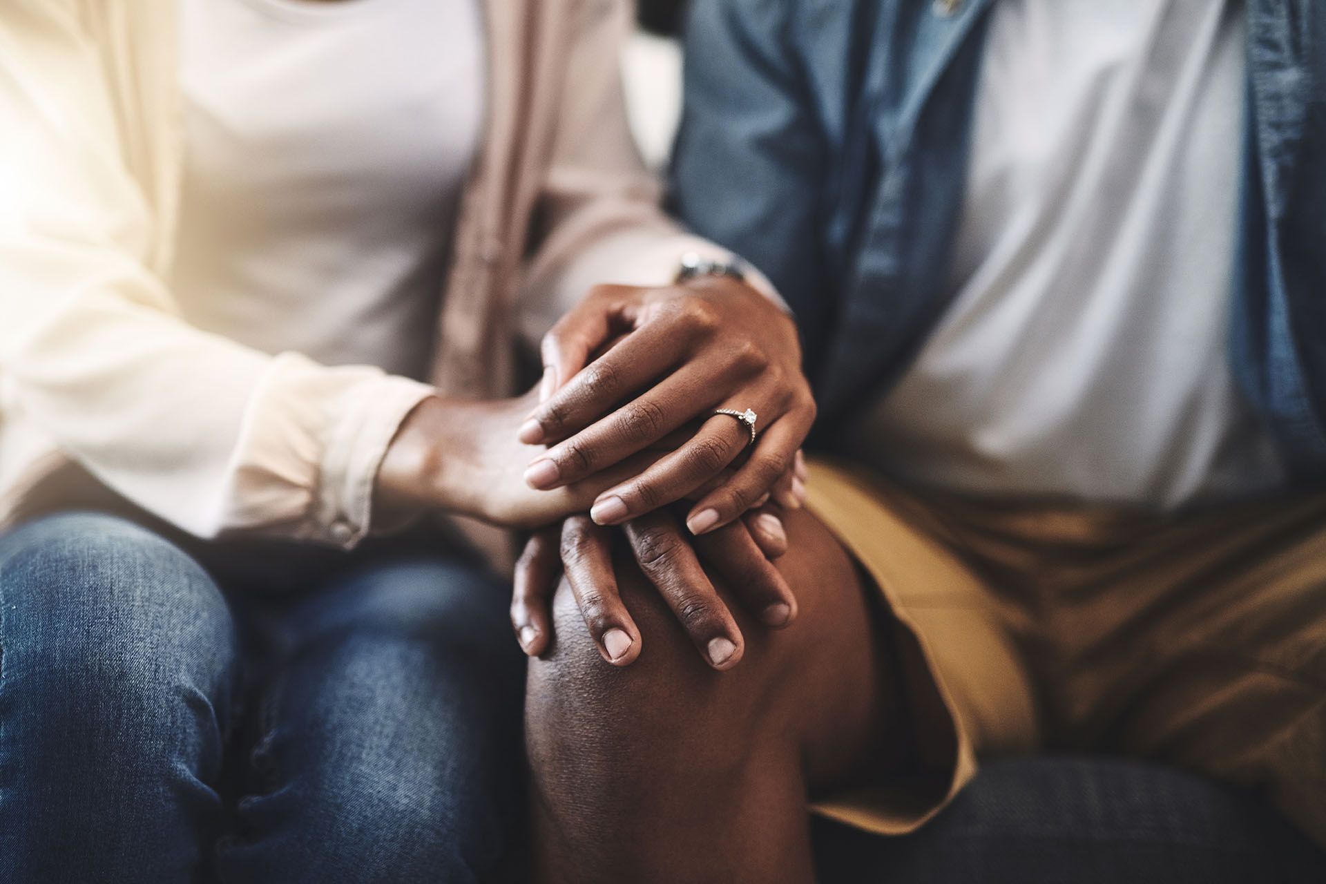 Couple holding hands; woman wearing ring, soft lighting.