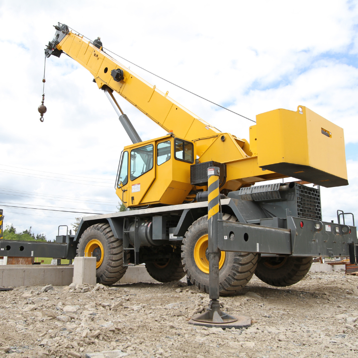 Yellow crane with wheels on construction site, boom extended, ready to lift.