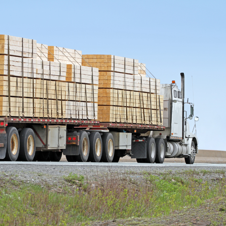 Semi-truck hauling stacks of lumber on a highway. Blue sky.