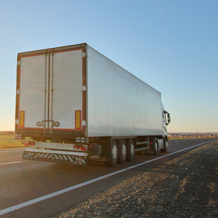 Semi-truck driving on a road under a blue sky.