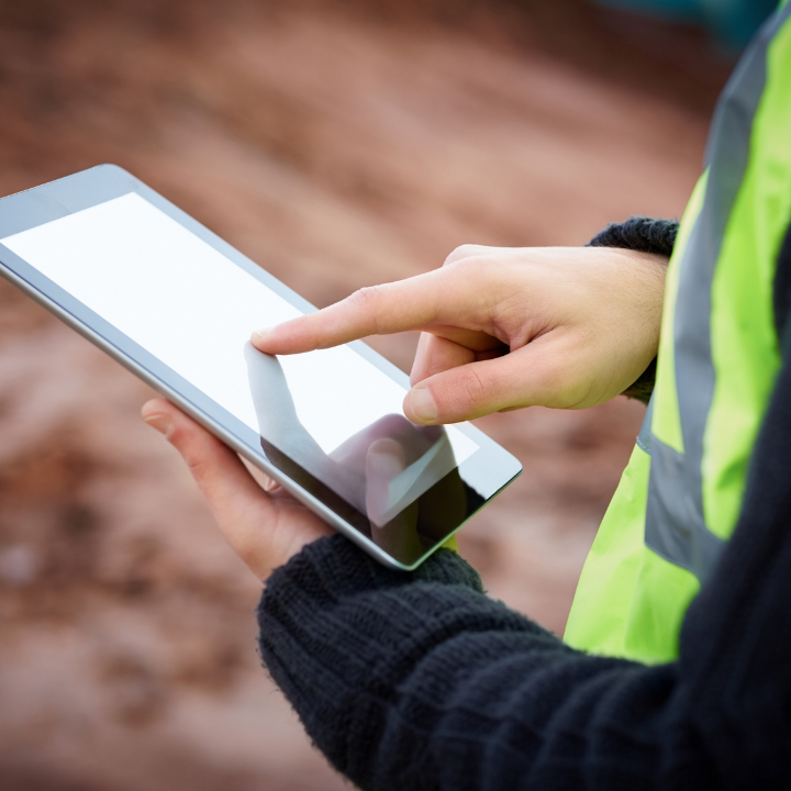 Person in a reflective vest using a tablet outdoors, pointing to the screen with a finger.