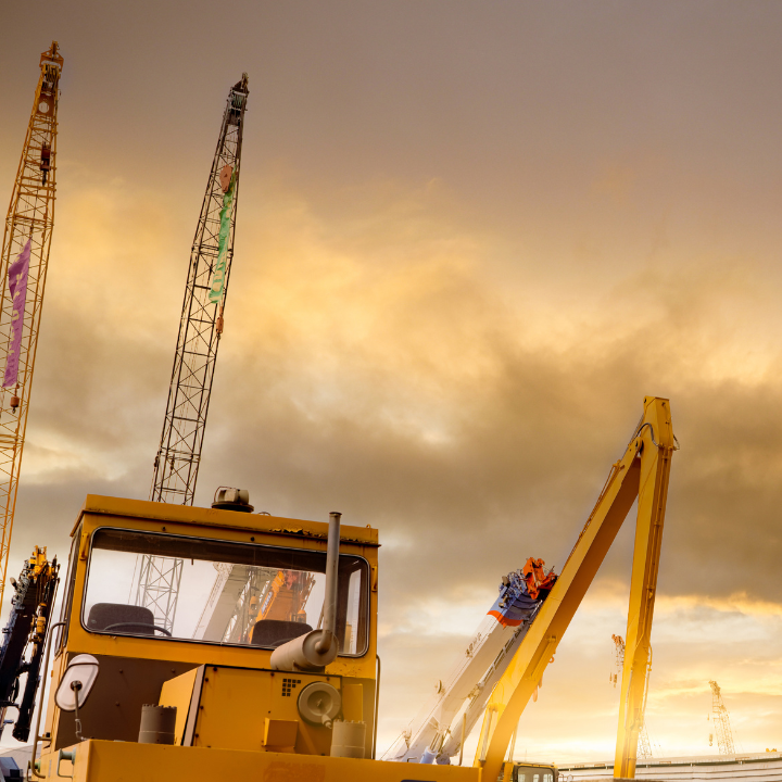 Yellow construction crane with two tall cranes against a cloudy sky.