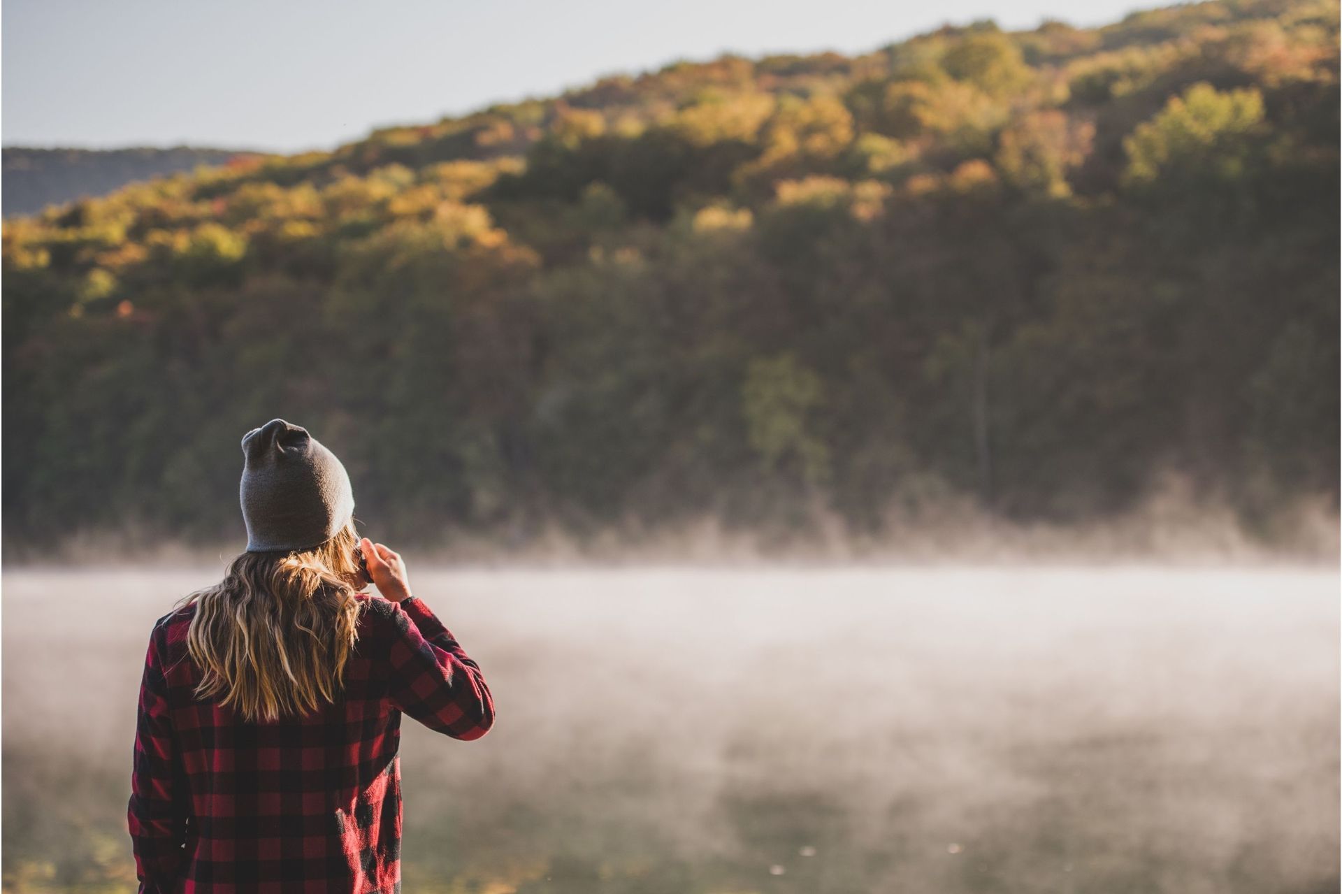 A person is sitting on a blanket holding a cup of coffee and a thermos.