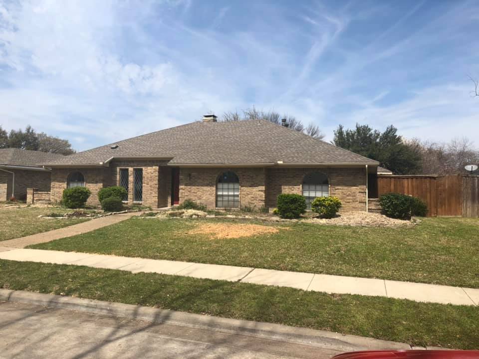 A brick house with a brown roof and a red car parked in front of it.