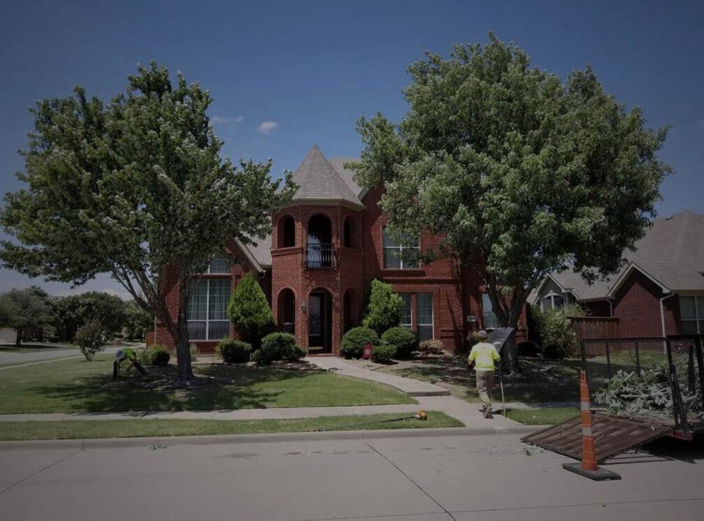 A man is walking towards a large red brick house with trees in front of it.