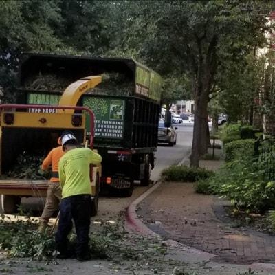 Two men are working on a tree chipper on the side of the road.