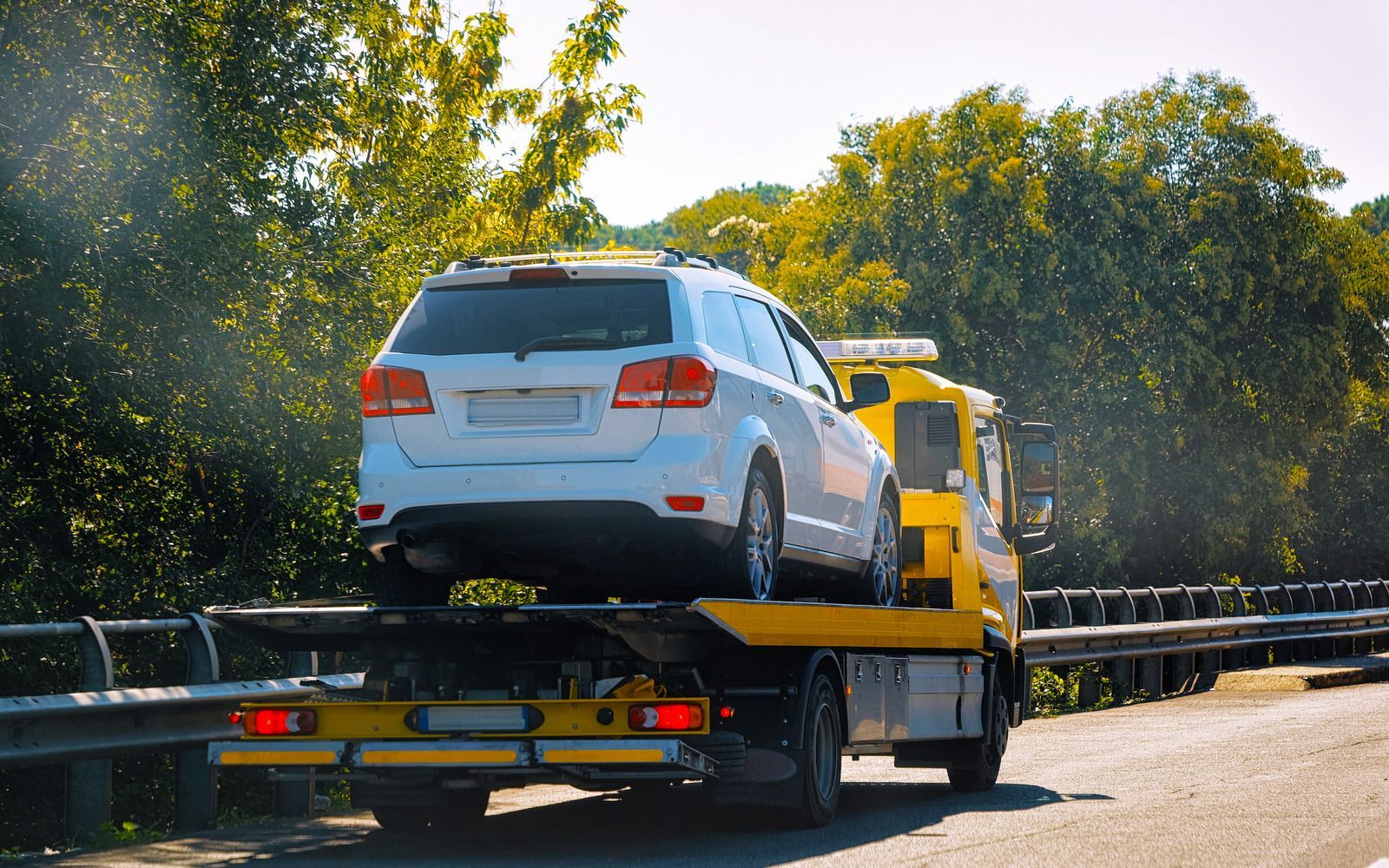 A white suv is being towed by a tow truck on a highway.