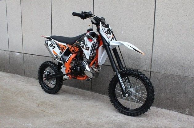 Una moto da cross arancione e bianca parcheggiata accanto a un muro grigio su una base di cemento.