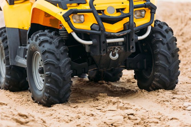 Un quad giallo fuoristrada attraversa un terreno fangoso, primo piano dei grandi pneumatici robusti.