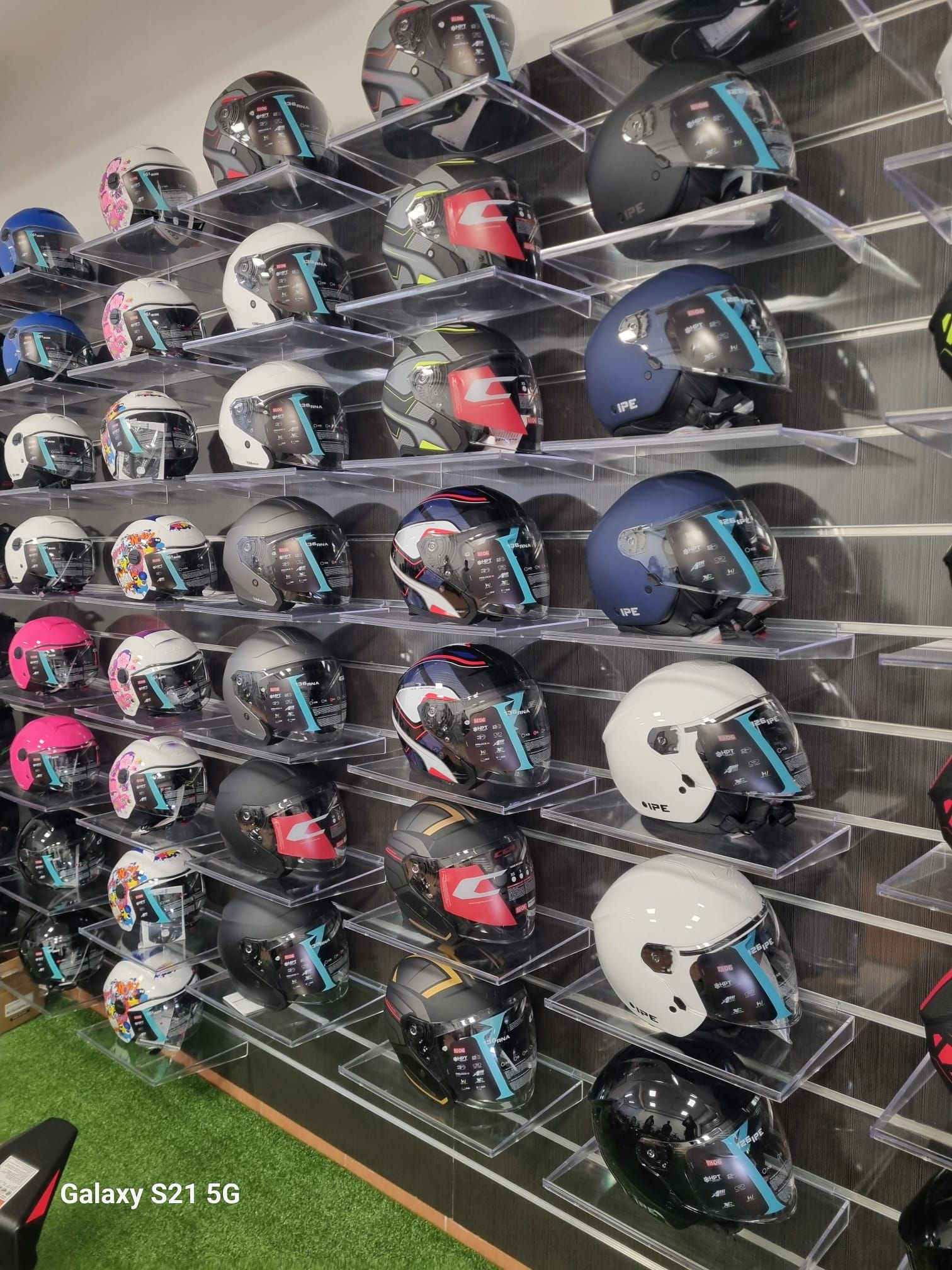 File di caschi da motociclista esposti su mensole a muro, nei colori nero, blu, bianco e rosso.