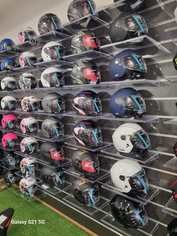 File di caschi da motociclista esposti su mensole a muro, nei colori nero, blu, bianco e rosso.