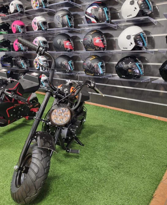 Una motocicletta nera all'interno di un edificio, davanti a una parete espositiva con caschi su degli scaffali.