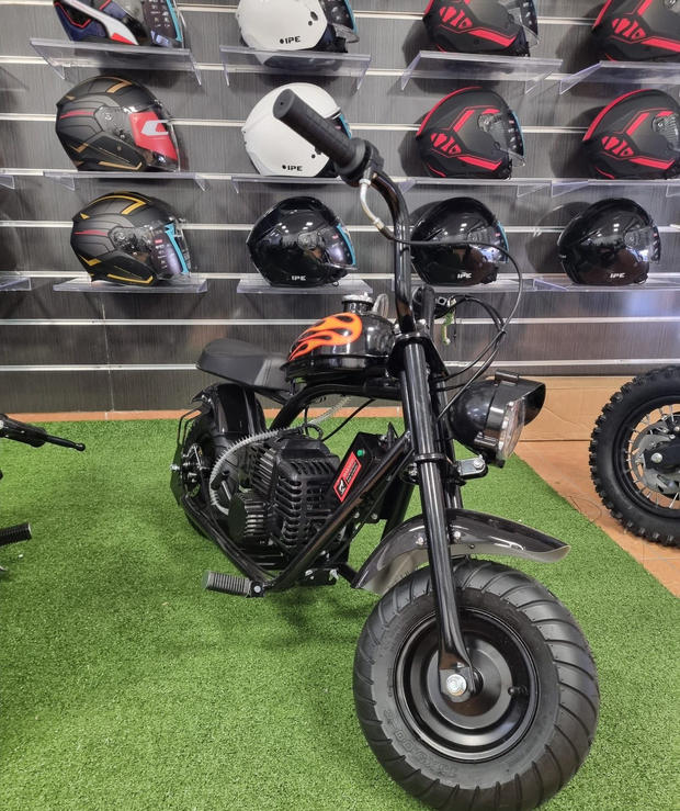 Mini moto elettrica nera su erba artificiale in un negozio di caschi, con i caschi esposti su scaffali a muro.