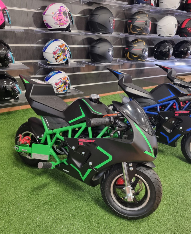 Due piccole motociclette sportive, verde e nera nella parte anteriore, esposte in uno showroom insieme a caschi sugli scaffali.