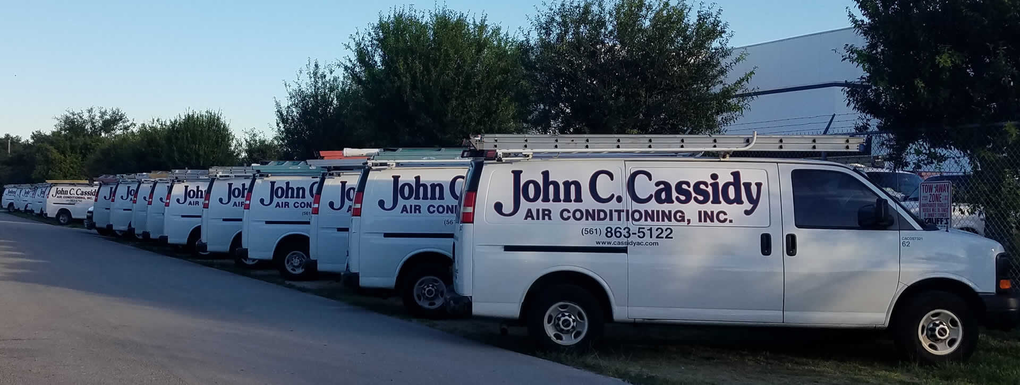 White vans with John C. Cassidy logo parked in a row on the side of a road.