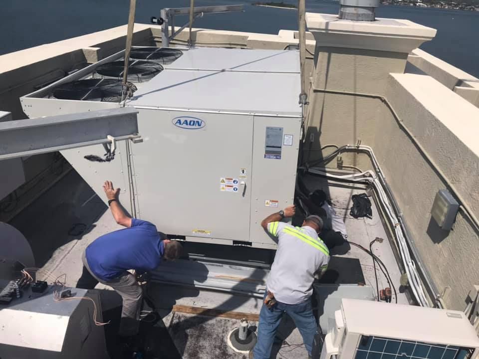 Two workers installing an HVAC unit on a rooftop with a waterfront view.