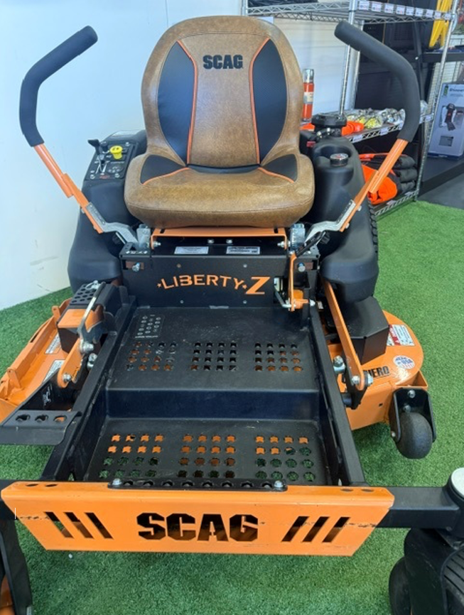 Orange SCAG Liberty Z zero-turn mower with black seat and handlebars, shown indoors on turf.