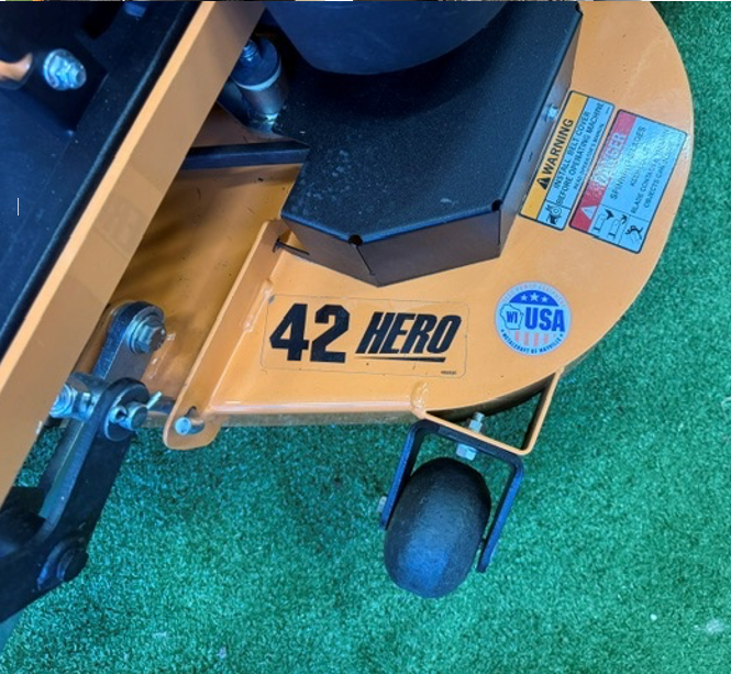 Close-up of a tan 42 HERO machine with a black wheel on green turf.
