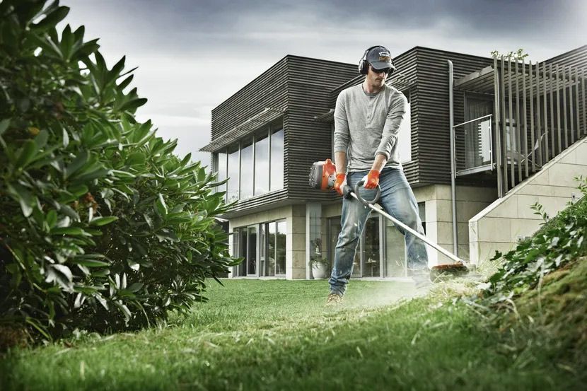 A Man is Using a Lawn Mower to Cut the Grass in Front of a House — Tuggerah Outdoor Power In Tuggerah, NSW