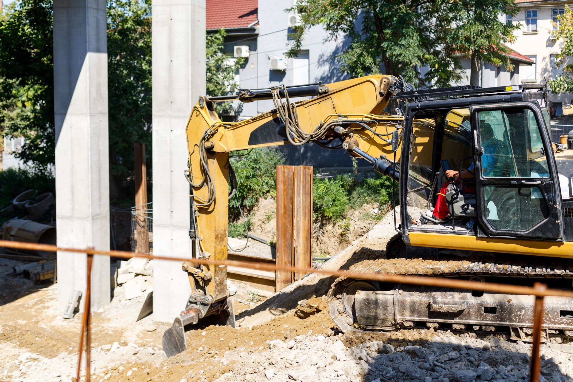 Yellow excavator digging near concrete pillars. Construction site.