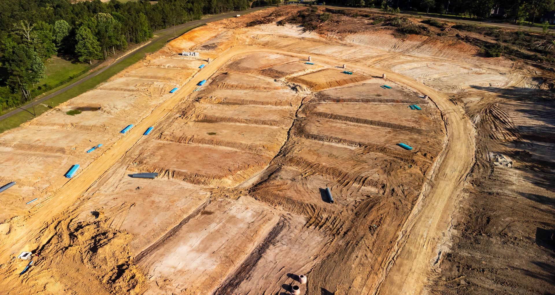 Aerial view of a cleared construction site with marked plots and access roads. Brown dirt and blue silt fences.