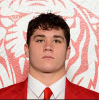 A young man in a red suit and tie is posing for a picture.