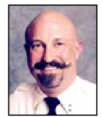 A bald man with a mustache and beard is wearing a white shirt and tie.