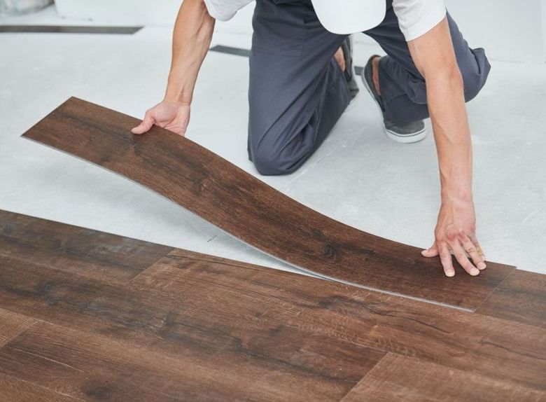 A man is kneeling down to install a wooden floor.